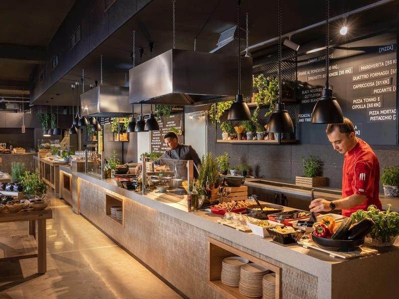 Moderne Restaurantküche mit langem Tresen, frischen Zutaten und zwei Köchen bei der Arbeit.