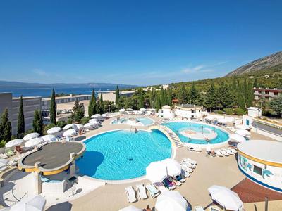 Round hotel pool with sun loungers and views of the sea and mountains.
