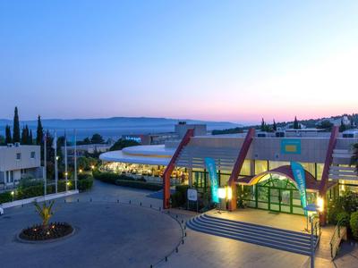 Hotel entrance at sunset with illuminated buildings and gentle landscape in the background.