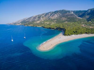 Vista aerea di un'isola sabbiosa con foresta fitta e mare azzurro chiaro vicino alle montagne.