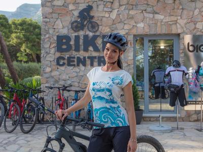 Woman wearing bike helmet with mountain bike in front of stone building with 'Bike Center' sign.