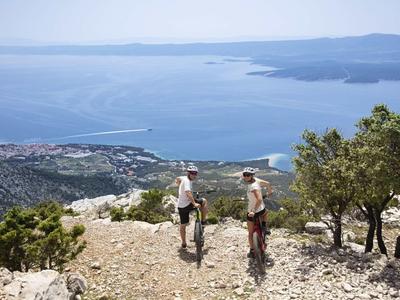 Two hikers on a mountain path overlooking the sea and coastal landscape.