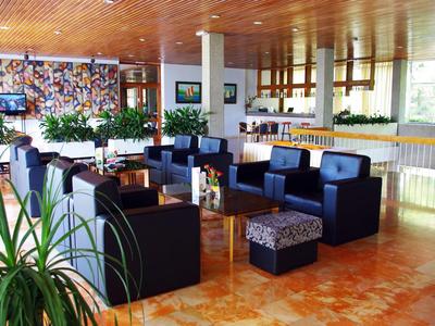 Moderní hotelový lounge s černými křesly, rostlinami a světlým dřevěným dekorem.