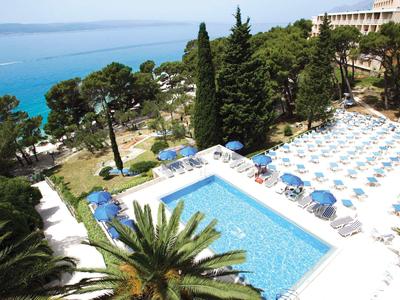 Blick auf einen Hotelpool mit Liegen und Blick aufs blaue Meer in der Ferne