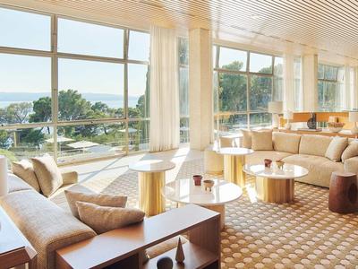 Heller Loungebereich mit bequemen Sofas, Teppichboden und großen Fenstern mit Blick aufs Meer.