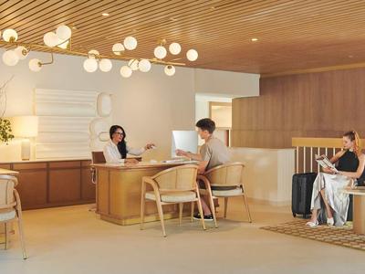 Moderne Hotellobby mit Holzdecke, runden Leuchten und Gästen an einem Empfangstresen.