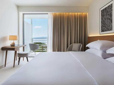 Modernes Hotelzimmer mit großem Bett, Schreibtisch, Fernseher und Fenster mit Vorhängen
