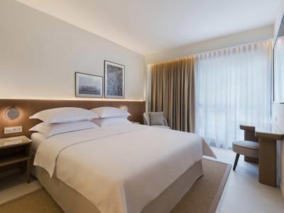 Moderní hotelový pokoj s velkou postelí, pracovním stolem a oknem se závěsy.