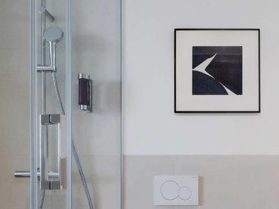 Moderní sprchový kout se skleněnou stěnou a uměleckým dílem na stěně koupelny.