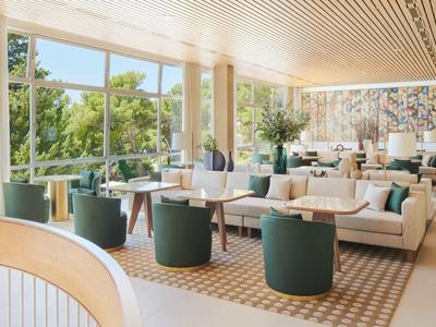 Helles Lounge mit grünen Sesseln, Sofas und großen Fenstern mit Waldsicht.