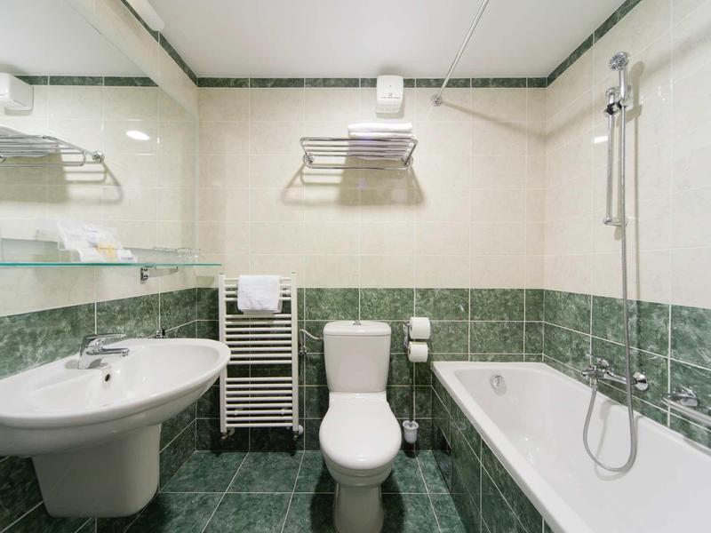 Moderní koupelna s toaletou, umyvadlem, vanou a vyhřívaným věšákem na ručníky.