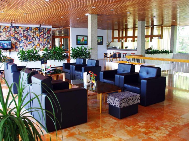 Moderní hotelový lounge s černými křesly, rostlinami a světlým dřevěným dekorem.