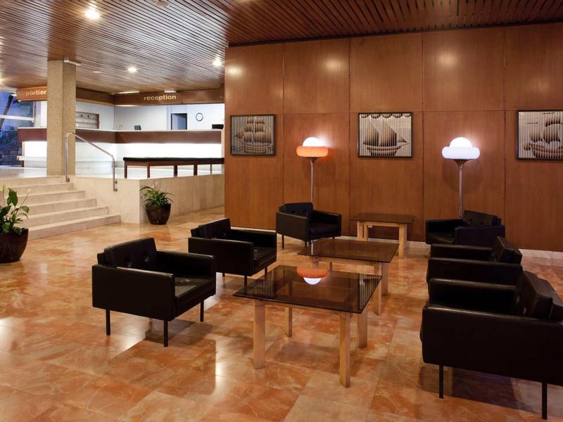 Moderní hotelová hala s černými křesly, dřevěnými stolky a dřevěnými obklady na stěnách.