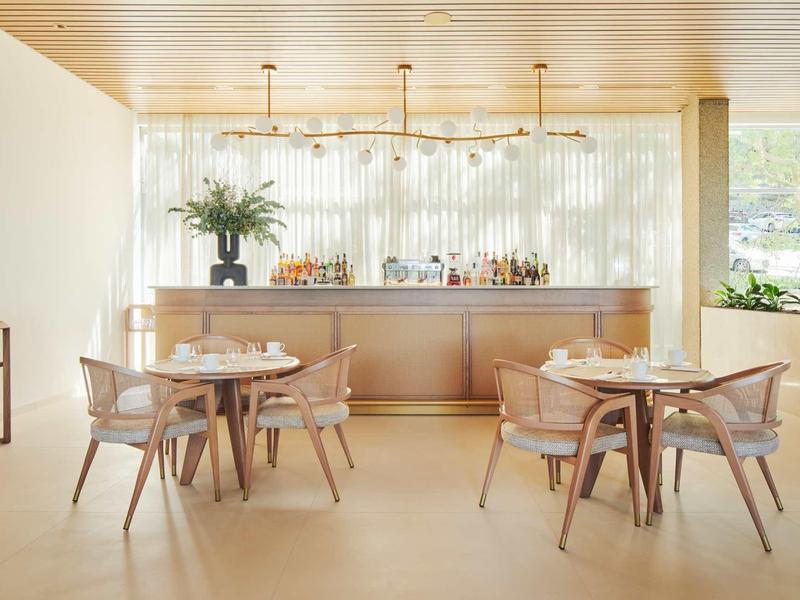 Jasná hotelová barová oblast se zlatým pultem, moderním osvětlením a kulatými stoly se židlemi.