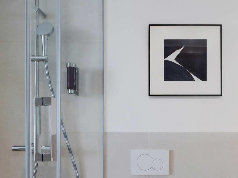 Moderní sprchový kout se skleněnou stěnou a uměleckým dílem na stěně koupelny.