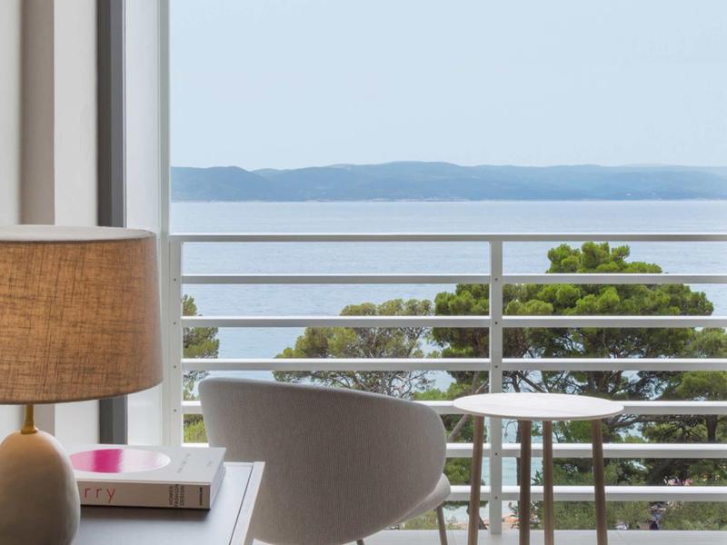 Moderní balkon s křeslem, stolem a výhledem na moře za jasné oblohy.