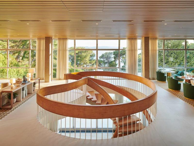 Světlá hotelová lobby s velkými okny a točitým schodištěm.