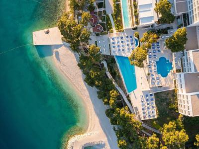Luftaufnahme eines Küstenresorts mit Pools, weißen Gebäuden, Sandstrand und türkisfarbenem Wasser.