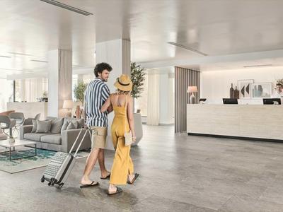 Un couple avec des valises marche dans le hall d'hôtel lumineux et moderne.