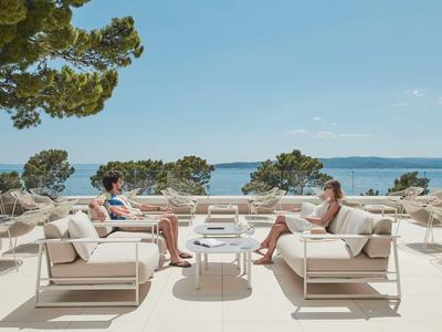 Deux personnes se détendent sur des canapés blancs avec vue sur la mer sur une terrasse d'hôtel.