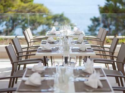 Tables élégamment dressées sur une terrasse avec vue sur une zone côtière boisée et la mer.
