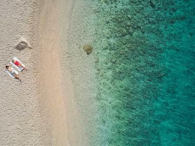Vue aérienne d'une plage avec de l'eau bleue et deux chaises longues avec des parasols.