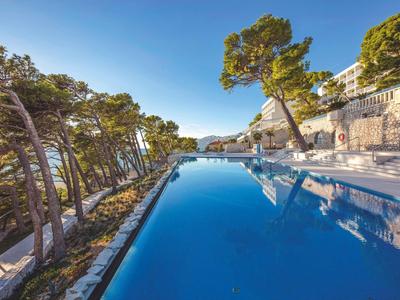 Piscina moderna en una terraza con vistas al mar, rodeada de árboles.
