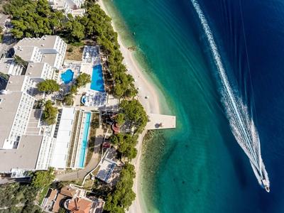 Vue aérienne d'un hôtel avec piscines à côté d'une plage de sable et mer claire avec un hors-bord