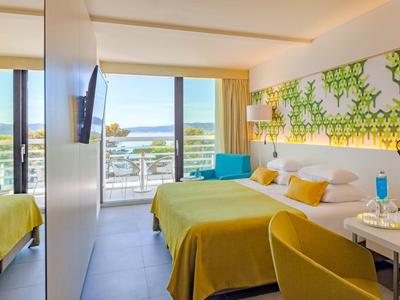 Chambre d'hôtel lumineuse avec couvertures jaunes, balcon et vue sur la mer.