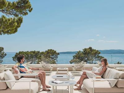 Dos mujeres se relajan junto a la piscina con vistas al mar bajo un cielo azul.