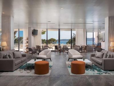 Moderna sala de hotel con sofás grises, otomanas naranjas y vista al mar
