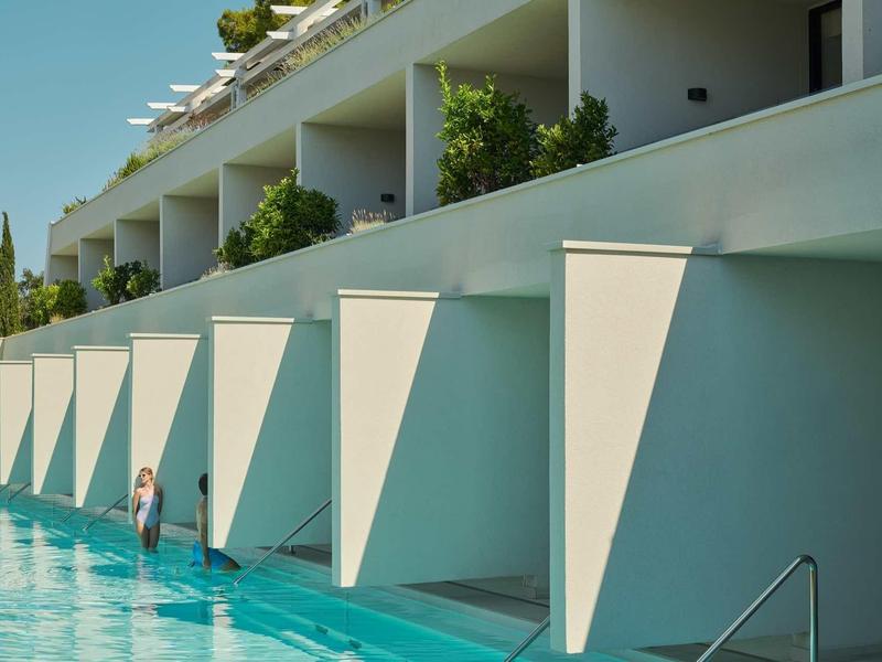 Bâtiment d'hôtel moderne avec piscine, alcôves privées et végétation verte.