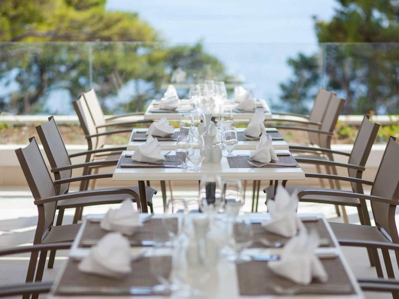 Tables élégamment dressées sur une terrasse avec vue sur une zone côtière boisée et la mer.