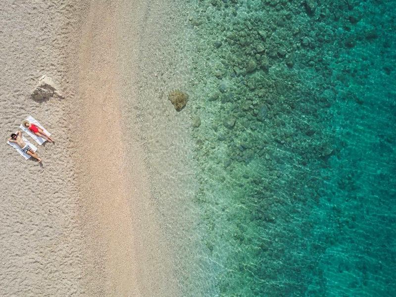 Vue aérienne d'une plage avec de l'eau bleue et deux chaises longues avec des parasols.