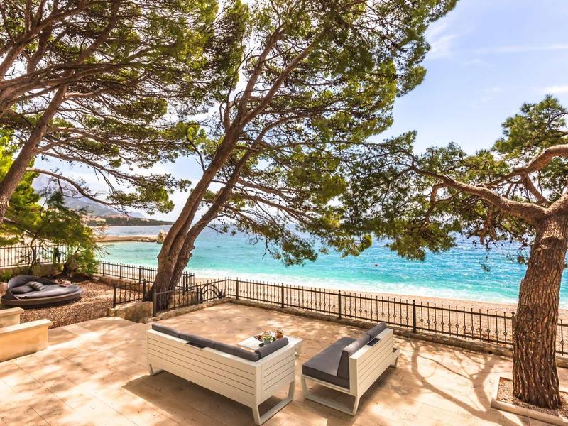 Terrasse avec sièges sous des arbres avec vue sur la mer bleue.
