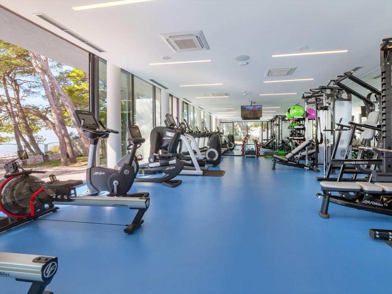 Salle de sport moderne avec grandes fenêtres donnant sur des arbres.