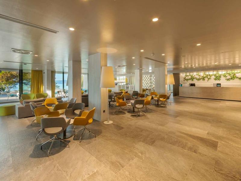 Hall d'hôtel moderne avec fauteuils jaunes et grandes fenêtres offrant une vue sur la mer.