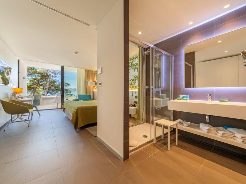 Espace moderne dans une chambre d'hôtel avec lit, bureau et salle de bain ouverte avec éclairage miroir.