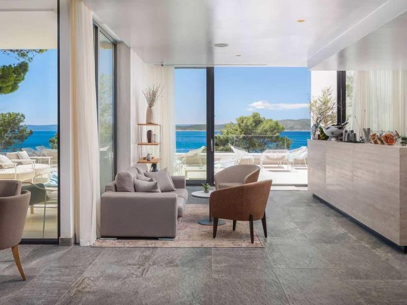 Chambre d'hôtel moderne avec fenêtres panoramiques donnant sur la mer et une terrasse.
