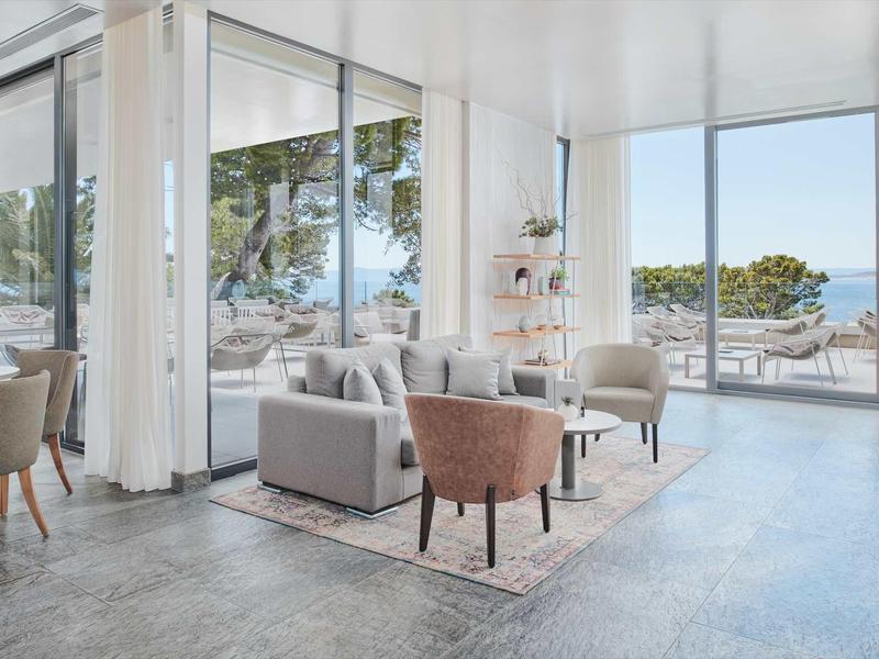 Salon lumineux avec coin salon, grandes fenêtres et vue sur la mer dans un hôtel moderne.