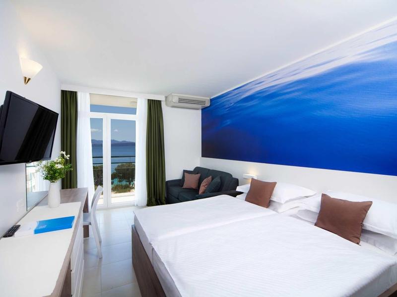 Nowoczesny pokój hotelowy z podwójnym łóżkiem, malowidłem ściennym i balkonem z widokiem na morze.