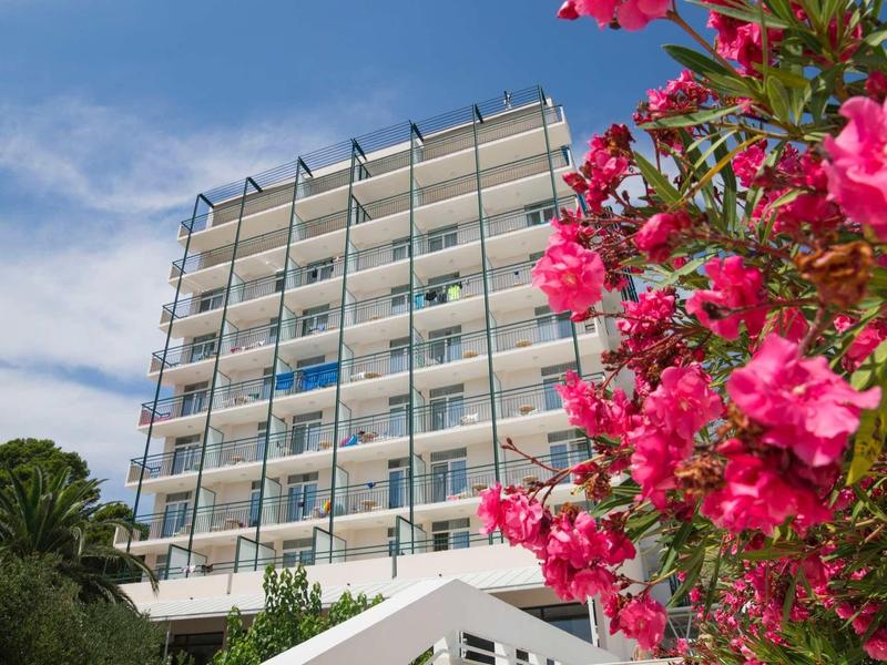 Nowoczesny budynek hotelu z balkonami i kwitnącym różowym oleandrem na pierwszym planie.