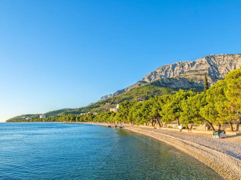 Piaszczysta plaża nad spokojnym morzem z drzewami i górami pod czystym niebieskim niebem