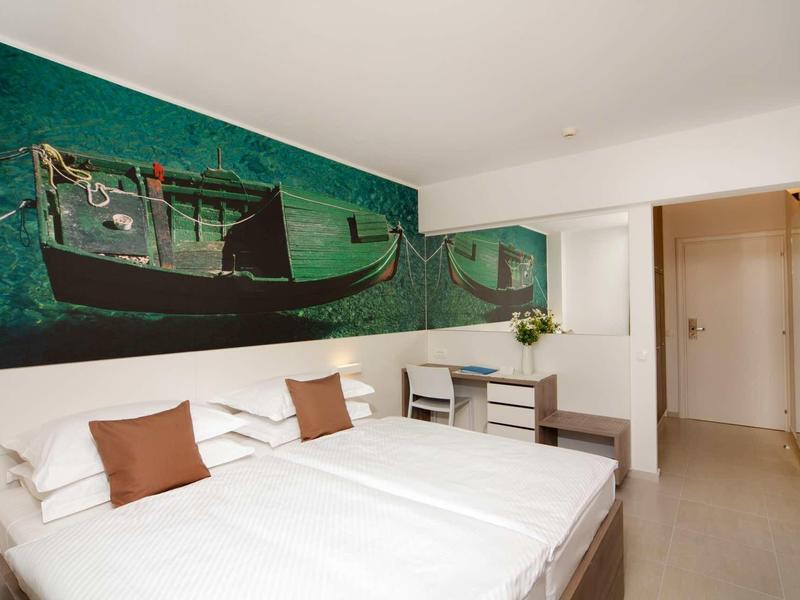 Nowoczesny pokój hotelowy z podwójnym łóżkiem, brązowymi poduszkami i muralem łodzi.