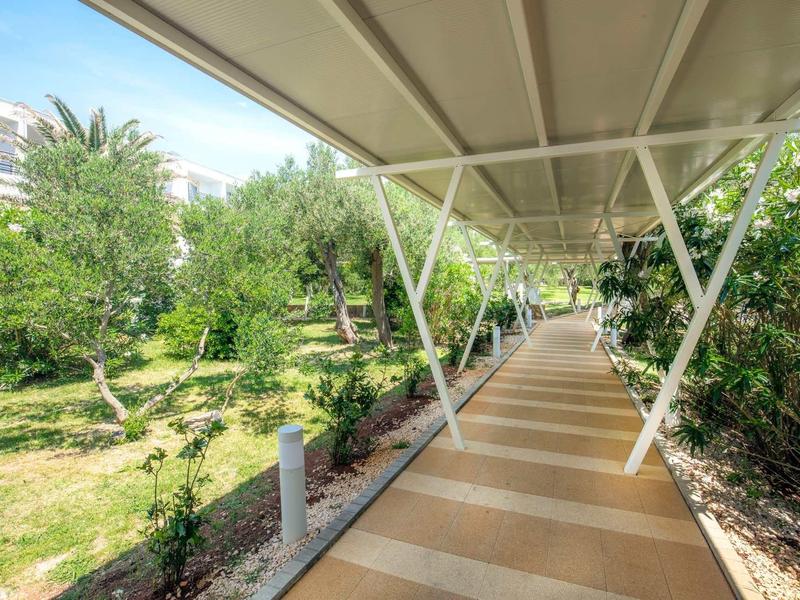 Zadaszony chodnik z roślinami i drzewami wzdłuż hotelu.