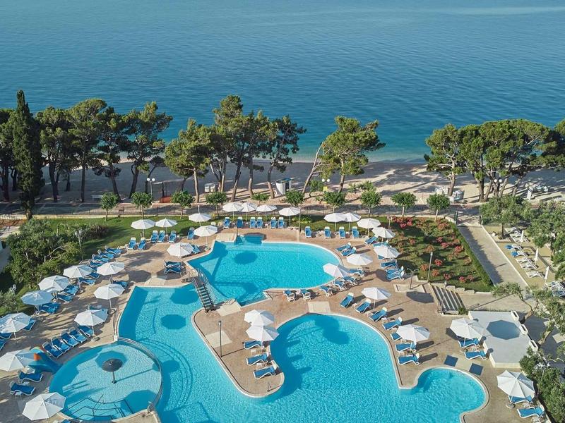 Kompleks hotelowy z kilkoma basenami, parasolami, leżakami i widokiem na morze.