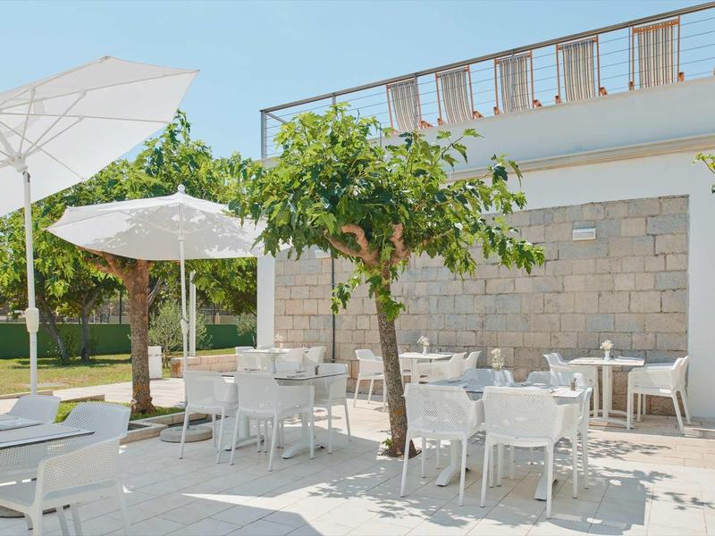 Słoneczny teren na zewnątrz hotelu z białymi stołami, krzesłami i dużymi parasolami.