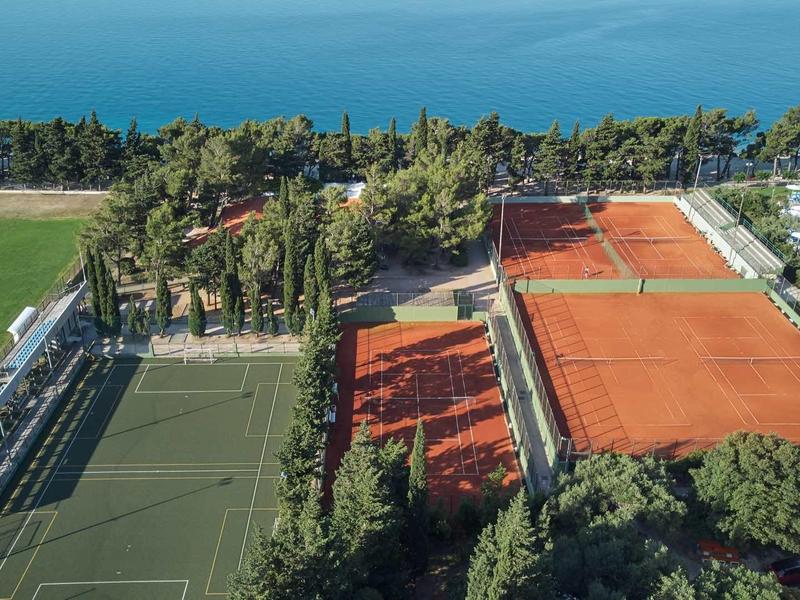 Widok z powietrza na kompleks sportowy z kortami tenisowymi, boiskiem piłkarskim i basenem blisko wybrzeża.