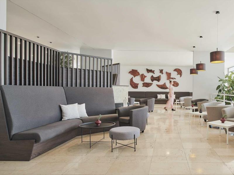 Nowoczesny hotelowy lounge z szarymi fotelami, stolikami kawowymi i dekoracyjną sztuką ścienną.