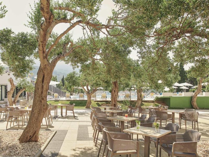 Strefa zewnętrzna hotelu z stołami, krzesłami i dużymi drzewami latem.